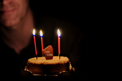 Close-up of illuminated candle on birthday cake with mature man in the background.