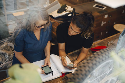 High angle view of female colleagues discussing over smart phone in retail store