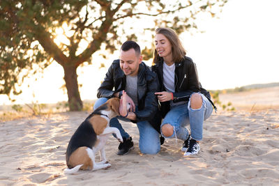 Full length of couple sitting with dog at beach
