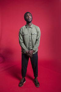 Portrait of young man standing against red wall