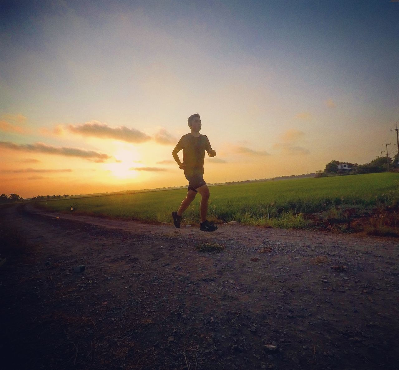 MAN STANDING ON FIELD AGAINST SKY DURING SUNSET