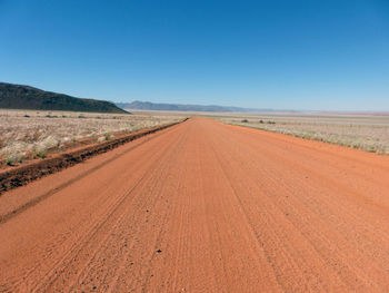 Dirt road passing through landscape against clear blue sky