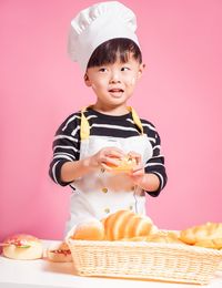 Cute boy holding bread crying while standing against pink background