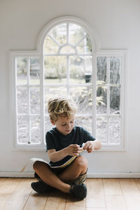 Boy with book sitting on floor against window at home