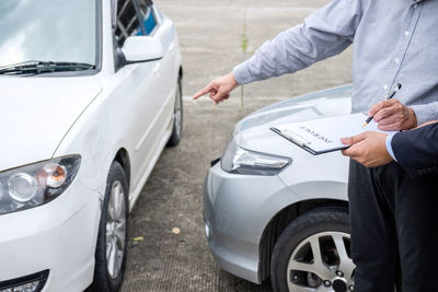 Midsection of owner pointing towards car while signing paper with agent