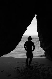 Silhouette man standing by rock formation at beach