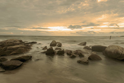 Rocks on beach against sky during sunset