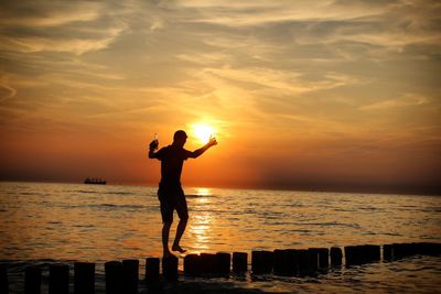 Silhouette walking on groyne in sea against sky during sunset