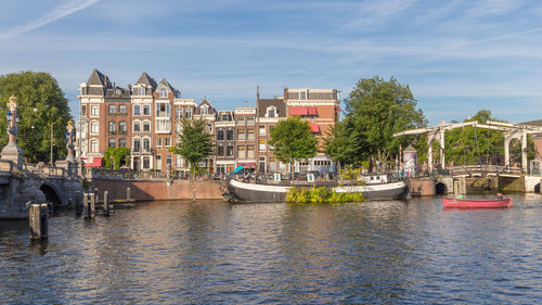 Sailboats moored on river by buildings in city against sky