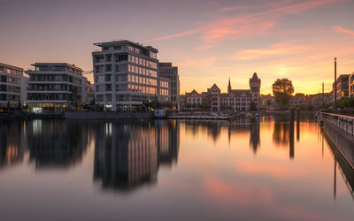 Reflection of buildings in river against sky at sunset