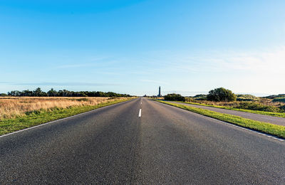 Country road amidst field against sky