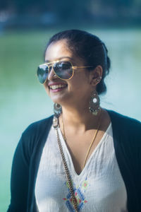 Close-up of cheerful young woman wearing sunglasses while standing against lake