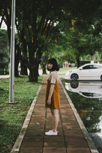 Side view portrait of young woman standing on footpath