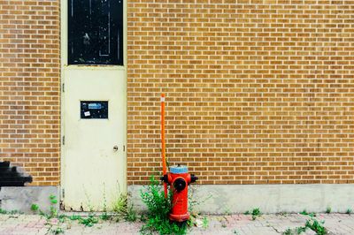 Red fire hydrant on sidewalk against brick wall