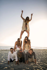 Cheerful friends making pyramid on beach against clear sky