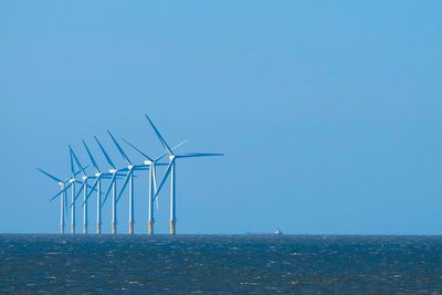 Wind turbines by sea against clear sky