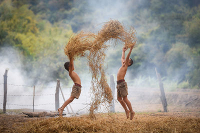 Shirtless boys playing with straws at farm