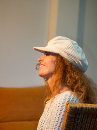 Profile view of smiling woman wearing hat sitting on chair at home