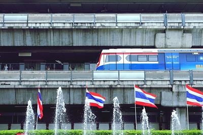 Low angle view of thai flags by fountain against elevated train