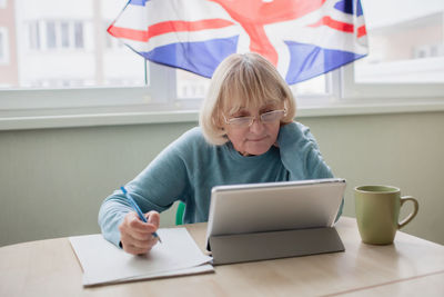 Senior woman learns english via internet with laptop, language classes for ukrainian refugee