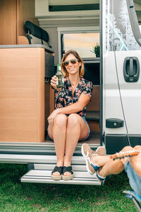 Woman showing beer bottle having fun with friends sitting at the door of their camper van