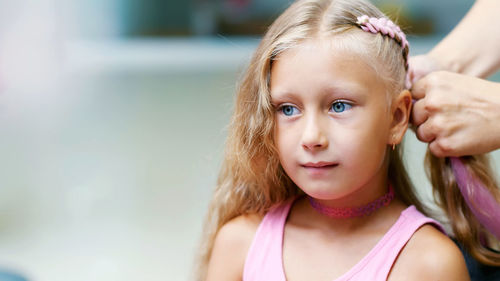 Beautiful blond girl, of seven years old, braided two pigtails, do a hairstyle with pink locks of