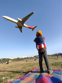 Rear view of man standing on airplane against sky