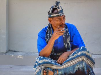 Man smoking cigarette while sitting against wall