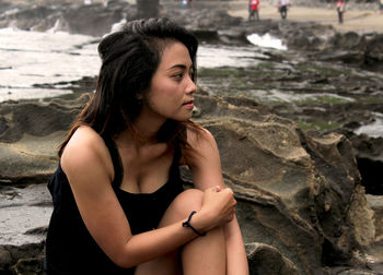 Thoughtful young woman sitting on rock at beach