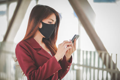 Young woman using phone while standing on railing