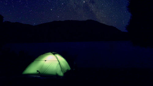 Illuminated tent by lake against sky at night