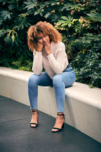 Portrait of young woman sitting on retaining wall by plants