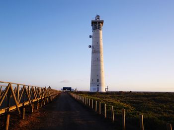 Lighthouse amidst field against clear blue sky