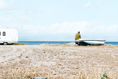 Man sitting in boat on the beach near his white camper van parked by the sea. sicily. ionian sea.