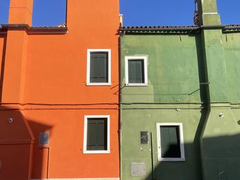 Low angle view of colorful green and orange houses against sky with shadows in burano, italy 