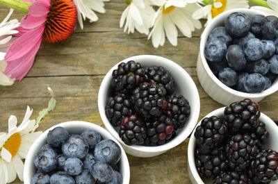 Blueberries and blackberries in small white ramekins with garden daisies on rustic wood table