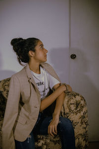 Woman looking away while sitting on sofa at home