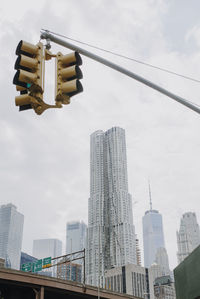 From below of traffic light hanging over road in new york city with contemporary skyscrapers and cloudy sky in background