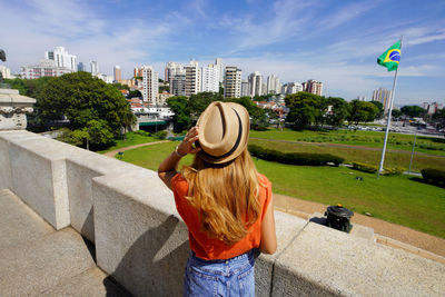 Brazilian girl looking the national flag with sao paulo cityscape on the background, brazil