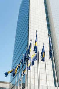 Low angle view of bosnia and herzegovinan flags and modern building against clear blue sky