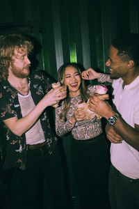 Cheerful young multiracial friends eating wrap sandwiches together at nightclub