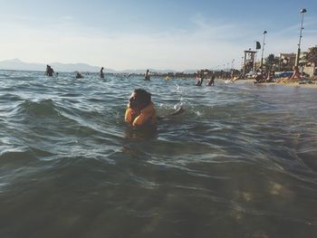 Boy wearing life jacket swimming in sea against sky