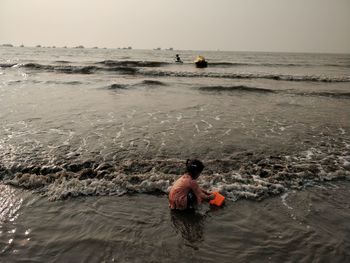 Rear view of boys on beach against sky