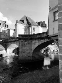 Arch bridge over river by buildings against sky