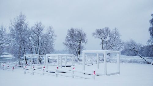 Bare trees on snow covered field against sky