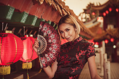 Portrait of smiling young woman in traditional clothing standing by lanterns