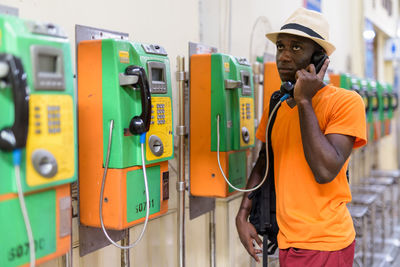 Man wearing hat talking on payphone