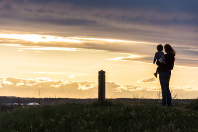 Couple standing on field against sky during sunset