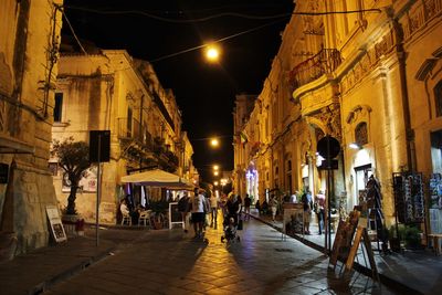 People on street amidst illuminated buildings in city at night