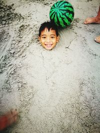 High angle portrait of playful boy buried in sand at beach